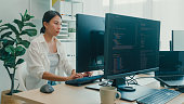Young Asian woman software developers using computer to write code sitting at desk with multiple screens work at office. Programmer development.