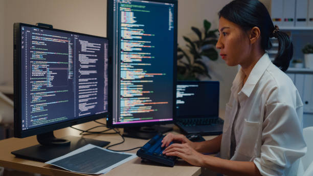 Young Asian woman software developers using computer to write code sitting at desk with multiple screens work in office at night. Programmer development. Young Asian woman software developers using computer to write code sitting at desk with multiple screens work in office at night. Programmer development concept. broadcast programming stock pictures, royalty-free photos & images