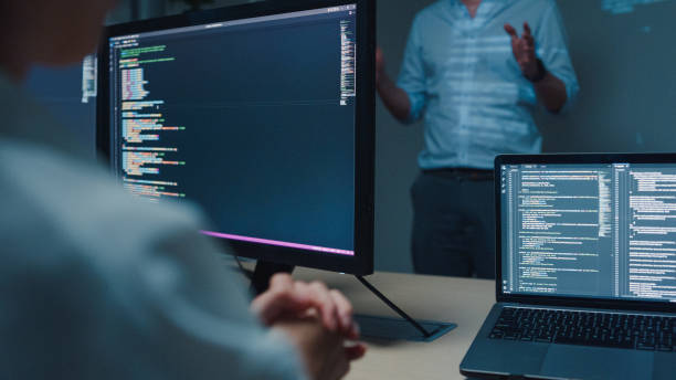 istock Closeup young Asian man software developers mentor leader manager talking to executive team analyzing source code in office at night. Programmer development. 1705602362