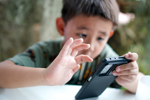Image of a young child paying attention while playing a mobile game during his free time during the holidays with his family.