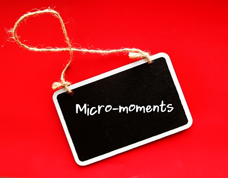 Chalkboard on red background with buzzword MICRO- MOMENTS, small moments of consumers before making a purchase decision - short precious times when brands get to interact with consumer