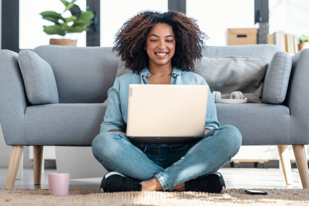 istock Happy young woman using her laptop while sitting on the floor at home 1705629771
