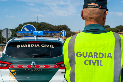 Badajoz, Spain. May 16, 2023. Civil guard agent equipped with his reflective vest, next to the patrol car on a road.