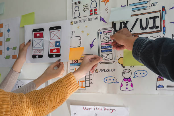 istock Image of a team of developers brainstorming UI and UX design ideas for a mobile app on a paper wireframe interface. Planning the user interface development team for an intuitive UI design. 1705637794