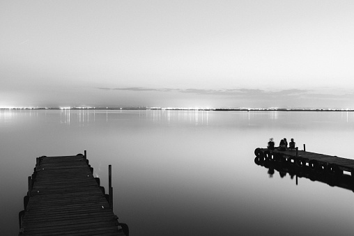 People resting relaxed on a pier on a lake at sunset with calm water