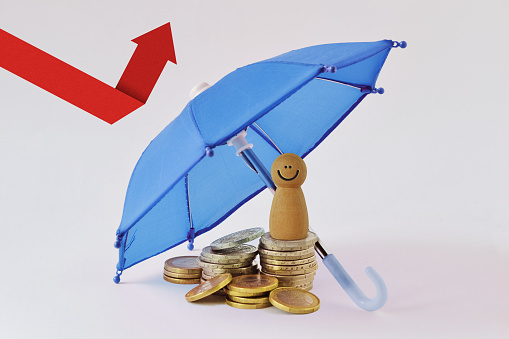 Wooden pawn on pile of coins under umbrella - Concept of economy and financial protection