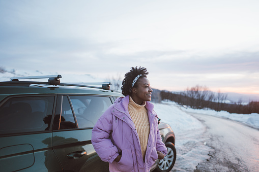 Photo of a young African American woman on a winter road trip with her car