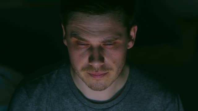 a man rubs his eyes at the screen at night