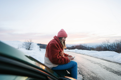 Photo of a young woman checking the maps on her mobile phone, while on a road trip with her car