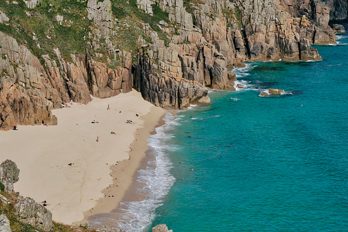 Late June afternoon views down onto Pedn Vounder Beach near Porthcurno, South Cornwall a few unrecognisable people on the beach enjoying the late afternoon sunshine.