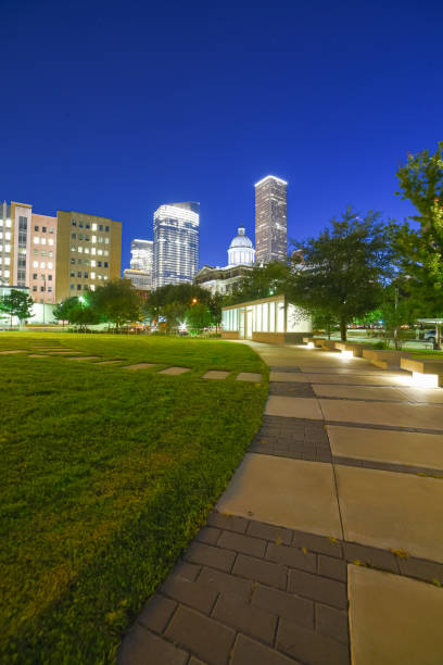istock Illuminated pathway concrete sidewalk at park square with downtown Houston skyscraper, capitol tower in background during evening blue hour 1705707254