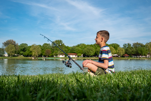 little blond child fishing fishes with fishing stick in natural pond