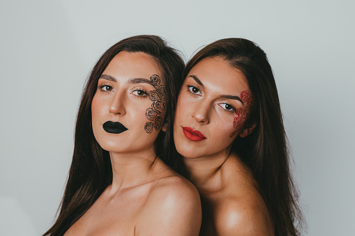 Portrait of two beautiful young women with face make-up art, studio shot in front of white background