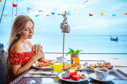 Woman on beach table enjoys delicious fruits - tasty watermelon, pineapple and exotic dragon fruit. Concept of enjoying a healthy breakfast on a tropical beach.