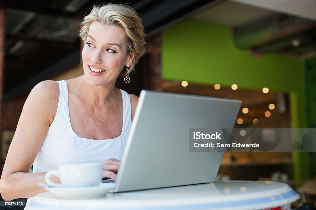 Femme à l'aide d'un ordinateur portable avec une tasse de café au Café - Photo de 45-49 ans libre de droits