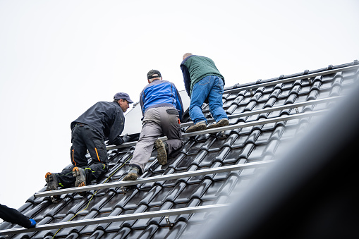 Three men during the installation of a photovoltaic system on the roof of a German single family home.