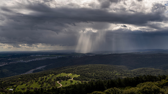 Panoramic view of sun rays shining through rainclouds showing the falling rain in Northern Israel looking towards the Mediterranean Sea from Muhraqa viewpoint.