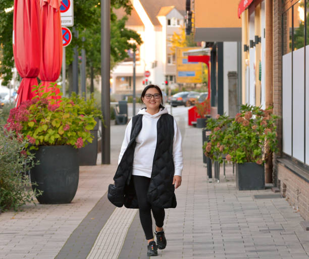 Street portrait of a beautiful Asian woman with long black hair walking through the city and smiling. A Buryat woman 55 years old is dressed in black and white casual clothes. stock photo