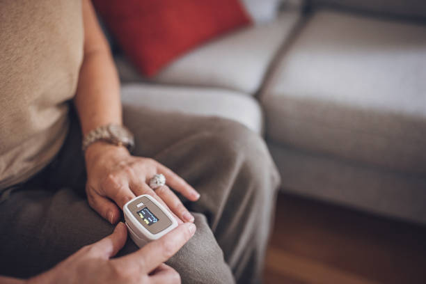 senior woman measuring saturation on her finger at home - taking pulse oximeter medical oxygen equipment human lung imagens e fotografias de stock