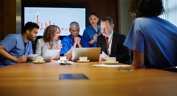 Multiethnic younger and elder business coworkers sitting in row together at large meeting table, talking, laughing, enjoying informal conversation, communication, networking