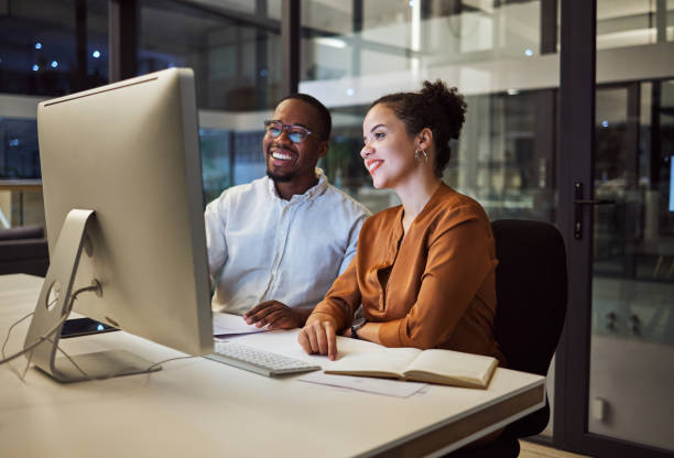 istock Night meeting, internet business and employees talking about web design on a computer in a dark office at night. African workers happy on company website and working overtime for partnership 1705796785