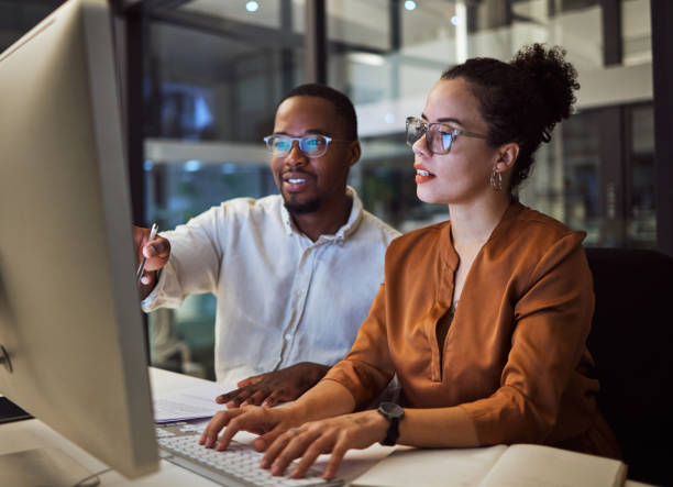 istock Night training, teamwork and employees planning marketing strategy in a dark office on computer at work. Corporate African man and woman talking about business collaboration during overtime together 1705796790
