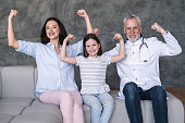Happy family doctor, girl patient and mother showing strong gesture by arms