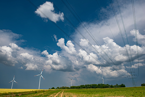 An approaching thunderstorm passes over the countryside with an overhead or high voltage power line with power poles and cables and fields in the foreground in oblique lower view