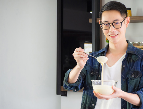 Cheerful efficient male young cook wearing casual cloth working on kitchen. Young man worker uses whisk and bowl for making mixing ingredients in a bowl. Kitchen tools and cooking concept
