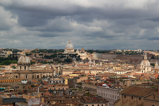 Photo with a panoramic view of the capital of Italy - the city of Rome with numerous churches and St. Peter's Cathedral in the center of the photo against the background of a stormy sky