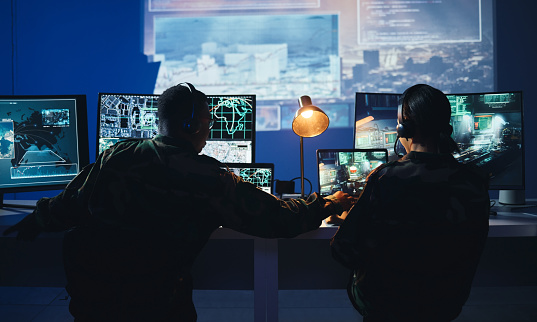 Army control room, computer and team in surveillance, help and collaboration in tech communication from back. Security, satellite map and man with woman at monitor in military office command center.