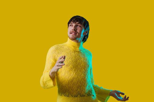 A waist-up shot of a young non-binary person dancing in a studio with a vibrant yellow background.