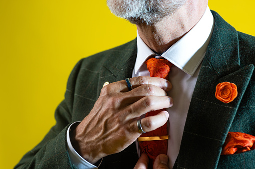 Close-up of an unrecognisable male adult adjusting tie. He is wearing a full piece suit with an orange tie.
