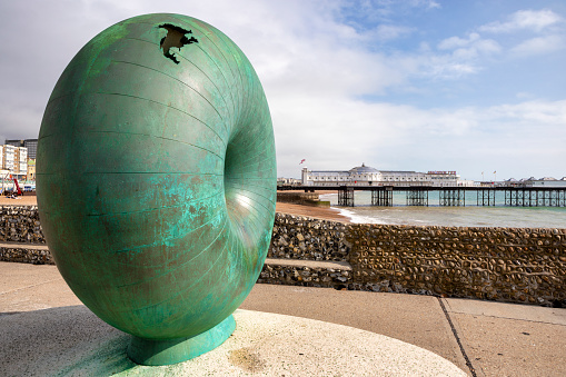 Brighton, United Kingdom - Sep 26, 2023: A public artwork by Hamish Black on Brighton seafront, UK. The sculpture is a circular donut shaped globe cast in bronze. Bronze sculpture on a groyne next to Brighton Palace Pier, Sussex, GB.