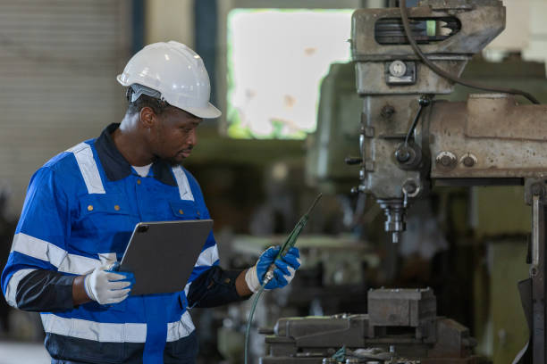 istock Male African American workers wearing uniform safety and hardhat using tablet working at machine in factory Industrial. Engineering worker man work machine lathe metal. Heavy industry concept. 1705883579
