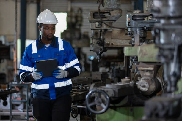 istock Male African American workers wearing uniform safety and hardhat using tablet working at machine in factory Industrial. Engineering worker man work machine lathe metal. Heavy industry concept. 1705883584