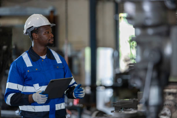 istock Male African American workers wearing uniform safety and hardhat using tablet working at machine in factory Industrial. Engineering worker man work machine lathe metal. Heavy industry concept. 1705883598