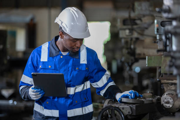 istock Male African American workers wearing uniform safety and hardhat using tablet working at machine in factory Industrial. Engineering worker man work machine lathe metal. Heavy industry concept. 1705885769