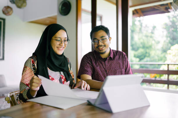 Happy Asian Hijab Woman Discussing With Finance Consultant At Home. Asian hijab woman and her finance consultant discussing together at home using digital tablet. Women in charge of finances. sharia stock pictures, royalty-free photos & images