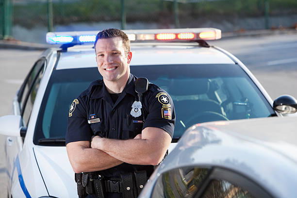 Police officer Police officer (20s) standing in front of cruiser. police force smiling officer stock pictures, royalty-free photos & images