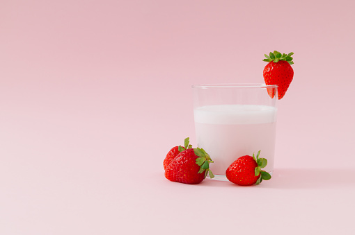 Creative composition made of milk drink with strawberry taste in glass cup decorated with red strawberries on pastel pink background. Minimal smoothie or milkshake concept. Healthy food for breakfast.