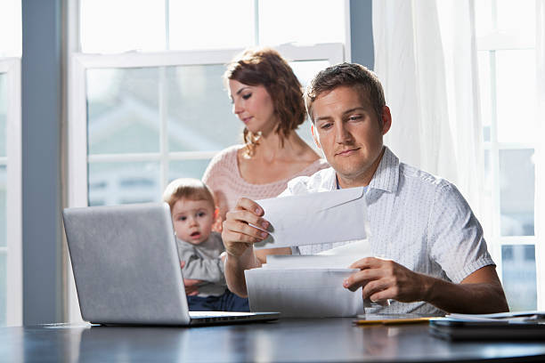 Family finances Young family with baby (8 months) at home.  Focus on father (20s) paying bills on laptop. Sc0601 stock pictures, royalty-free photos & images