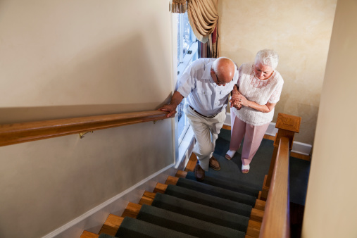 Senior woman helping husband (80s) climb staircase.