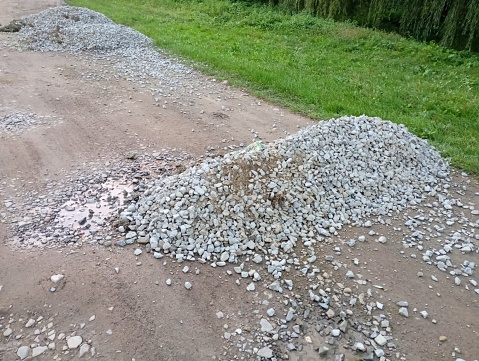 A pile of crushed stone is spilled on the field dirt road next to the shoulder. Repair of a field road in the countryside.