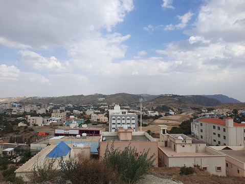 Beautiful daytime sky view of Al Bahah city in Saudi Arabia. City buildings, hills and clouds are visible in the background.