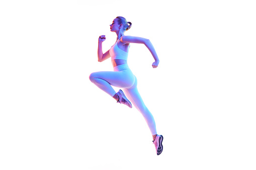 Side view portrait of young spory woman running in action isolated against white background in neon light. Warming-up. Concept of sport, fitness, healthy lifestyle, strength, youth, ad. Copy space