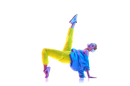 Side view portrait of young girl training, raising one leg in trendy sport outfit and headphones looking at camera in neon light. Concept of sport, fashion, active lifestyle, motion, youth. Copy space