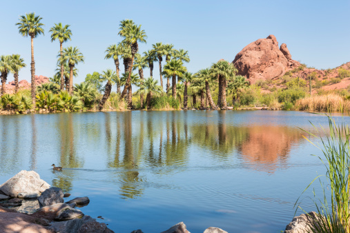 A red sandstone butte reflects in a small fishing lagoon in Papago Park, Phoenix, Arizona.