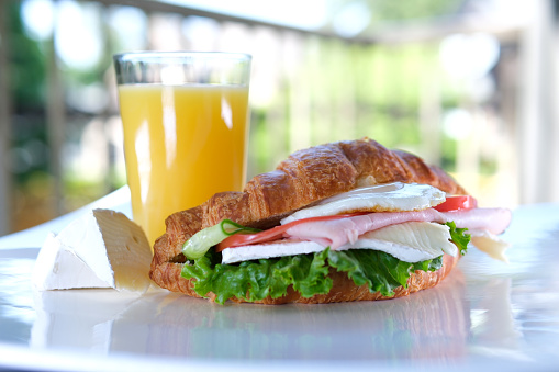 croissant with balyk and cucumber Lettuce leaves tomato delicious breakfast with cheese and orange juice on white plate bacon layers in sandwich on the balcony. delicious food lunch snack