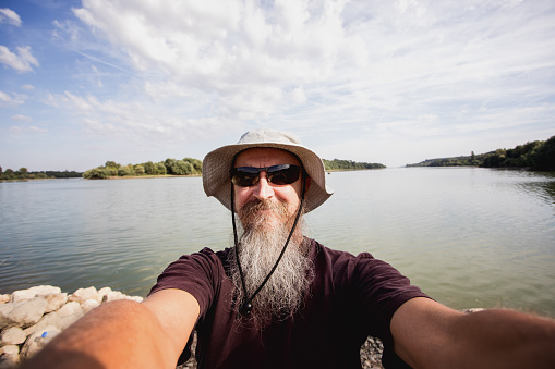 50 year old sports fisherman at fishing ground on Danube river smiling at camera, selfie